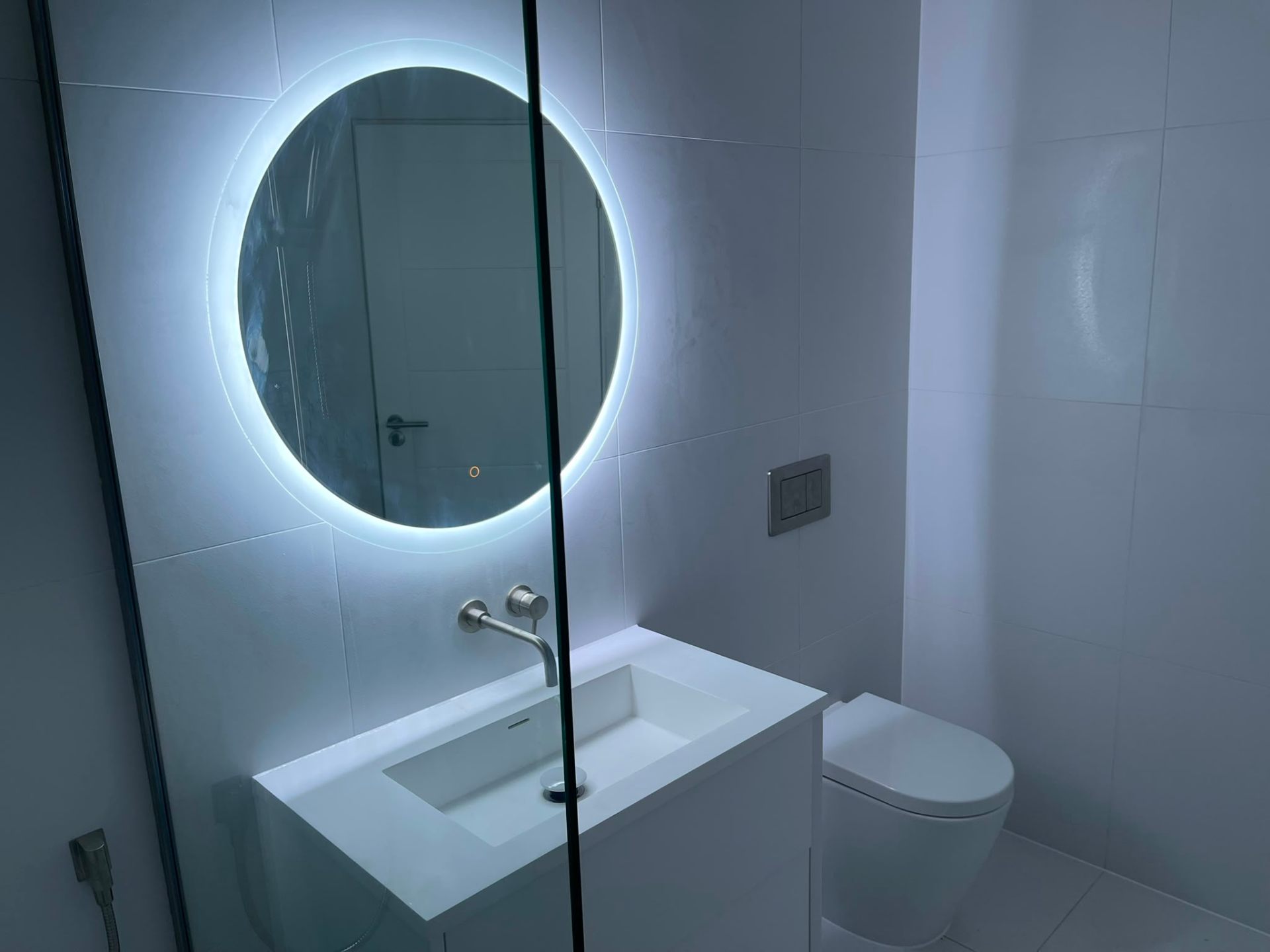 Feature-wall bathroom installation with dark tiling, backlit mirror and wall-hung WC, Surrey