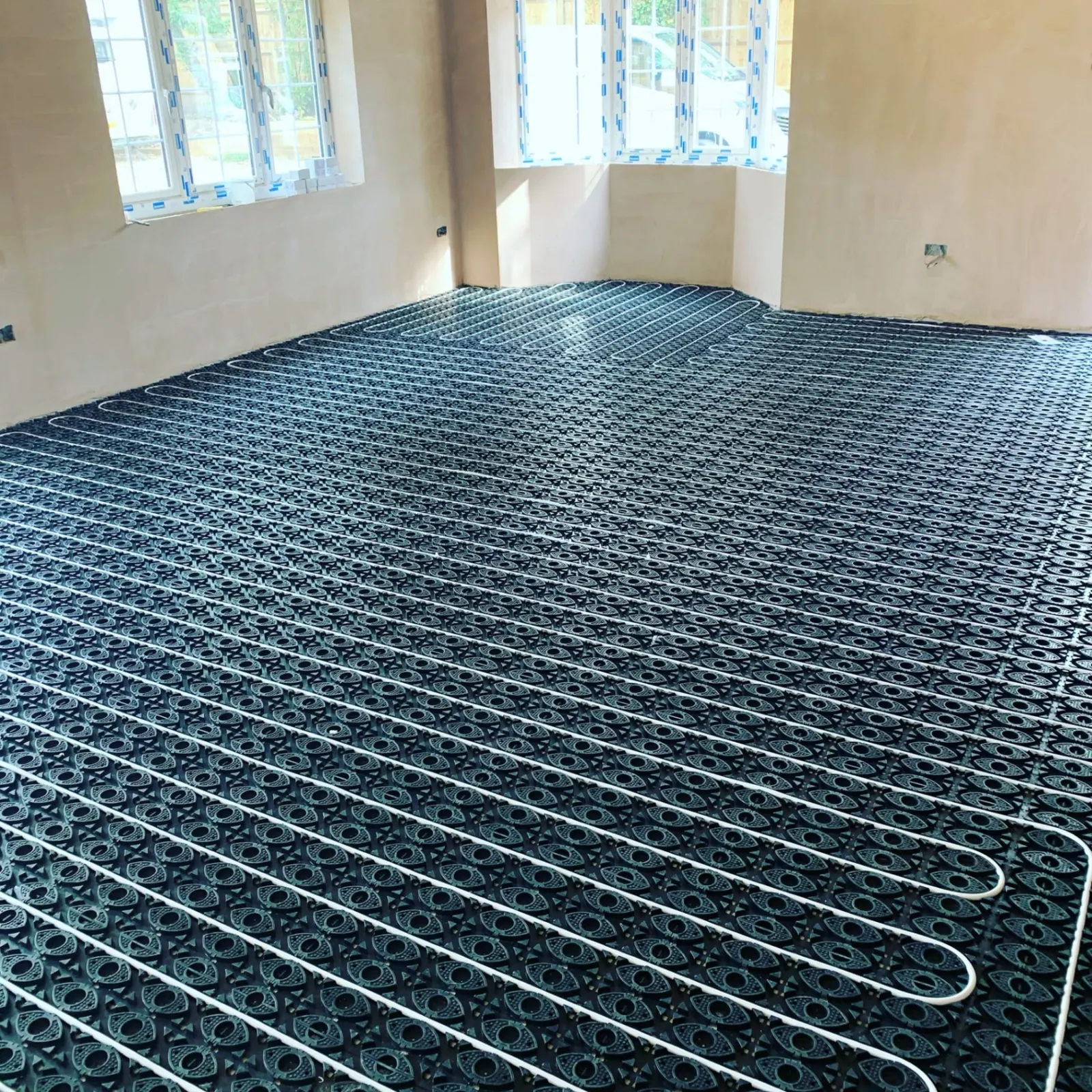 Underfloor heating manifold and pipe grid installed across a plastered new-build room in Ashford